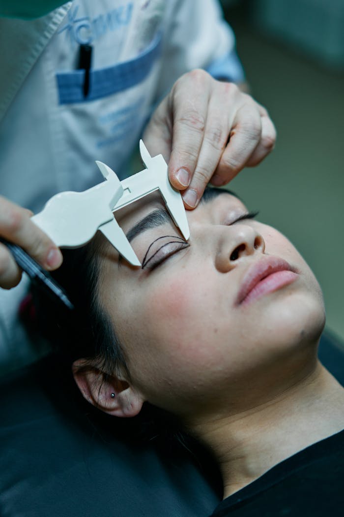 pexels-photo-7585311 A surgeon measures a patient's eyelid for blepharoplasty preparations.